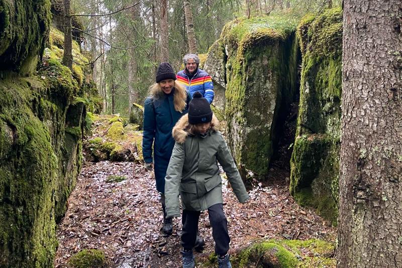 Tre personer går langs en sti mellom mosekledde steiner i skogen.