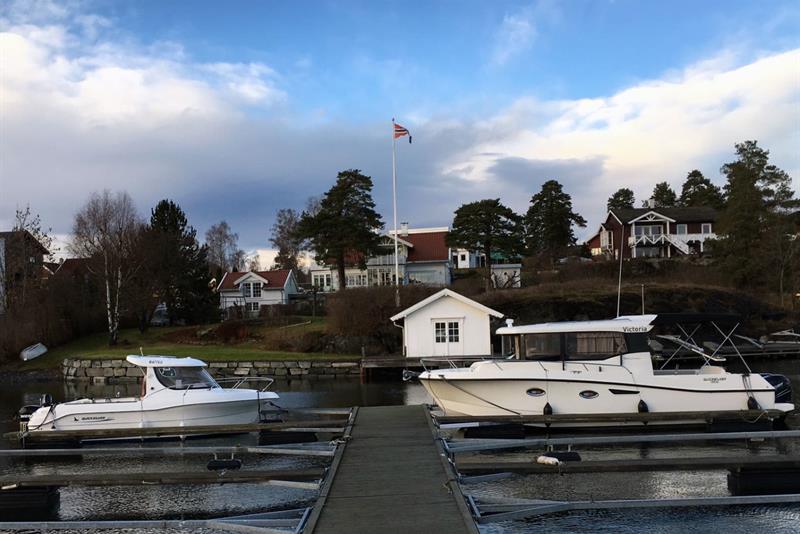 brygge med båter fortøyd i havnen og hus i bakgrunnen