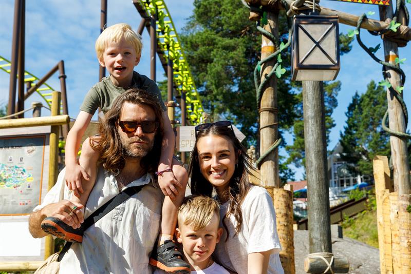An adult and three children posing in front of a roller coaster